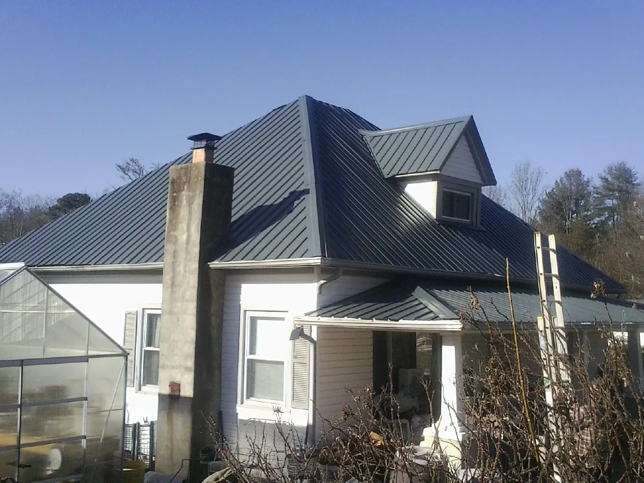 Dark blue standing seam metal roof on a white farmhouse with dormer — Slate & Tile Roof Repair by Roofing Brothers in Bennet