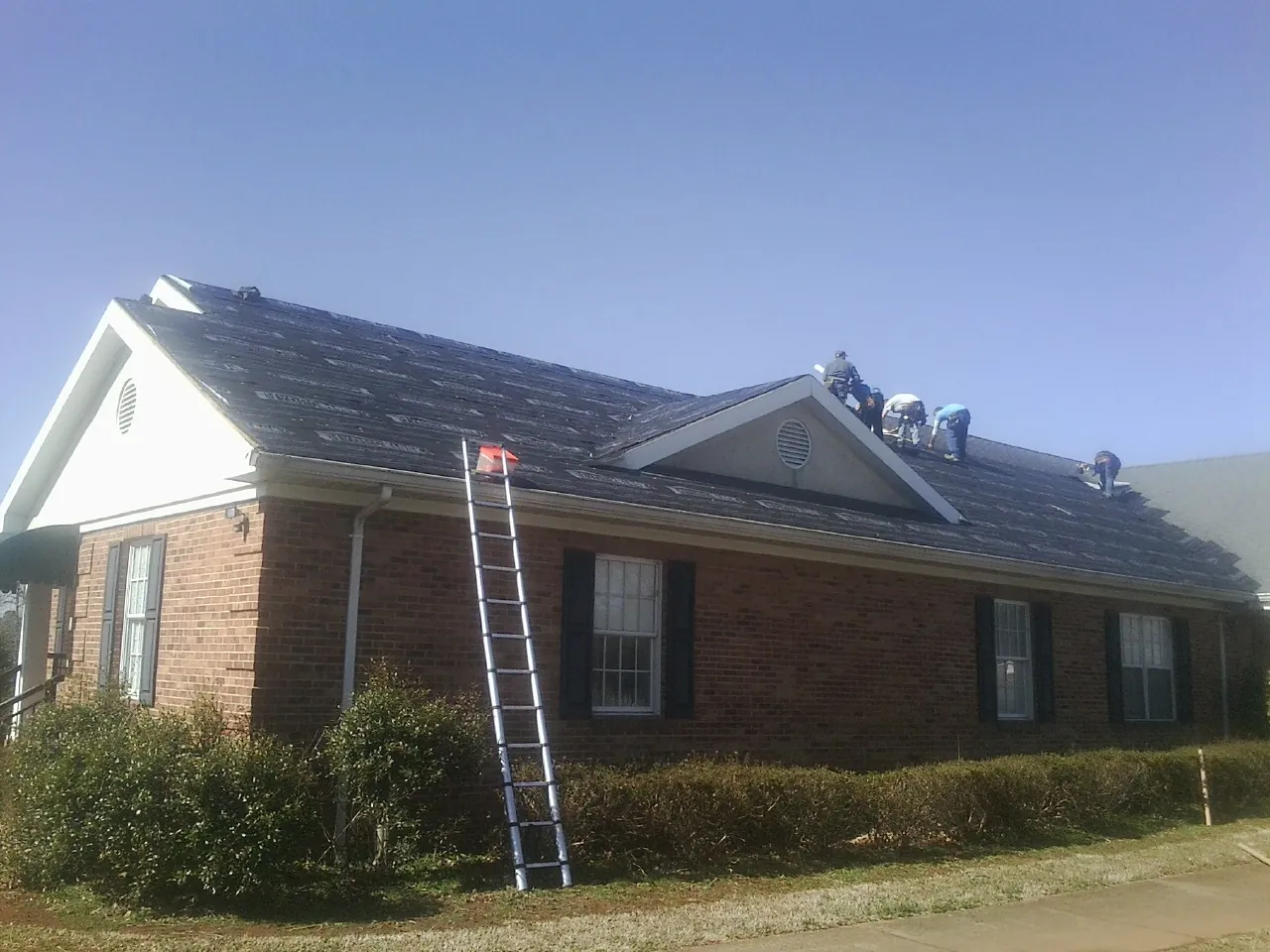 Crew tearing shingles off a brick ranch roof with a ladder set — Metal Roof Repair work by our crew in Bennet
