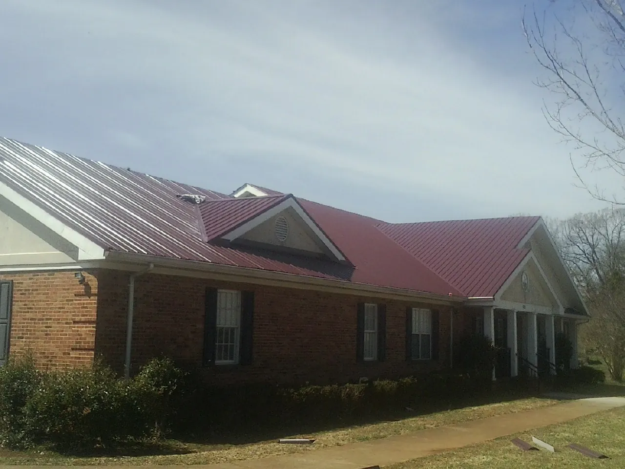 Red metal roof with gabled entries on a long brick building, from a Hail Damage Roof Repair job in Bennet
