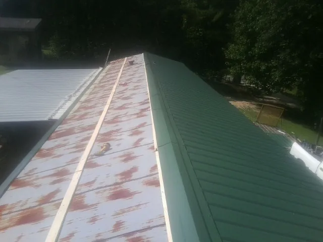 Old rusted panels beside newly installed green metal roofing — Wind Damage Roof Repair by Roofing Brothers in Bennet