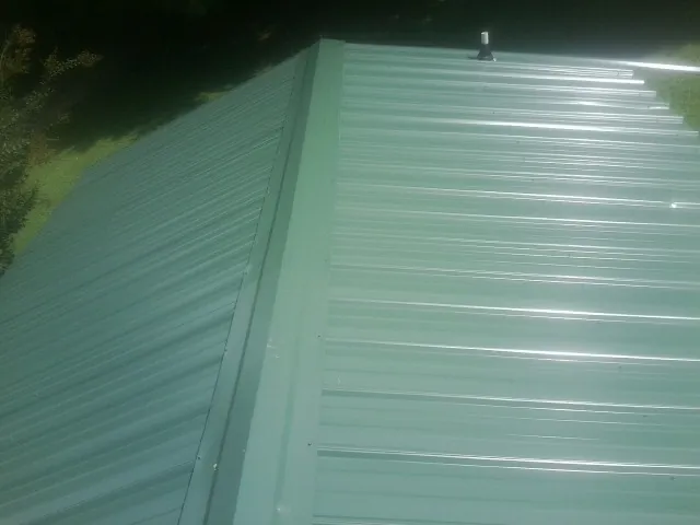 New green metal panels meeting at the ridge of a roof — Flat Roof Repair work by our crew in Bennet