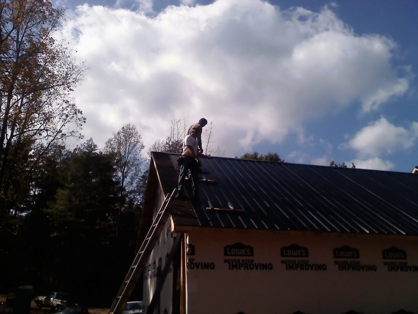 Roofer fastening dark metal panels high against a cloudy sky, from a Roof Inspection job in Bennet