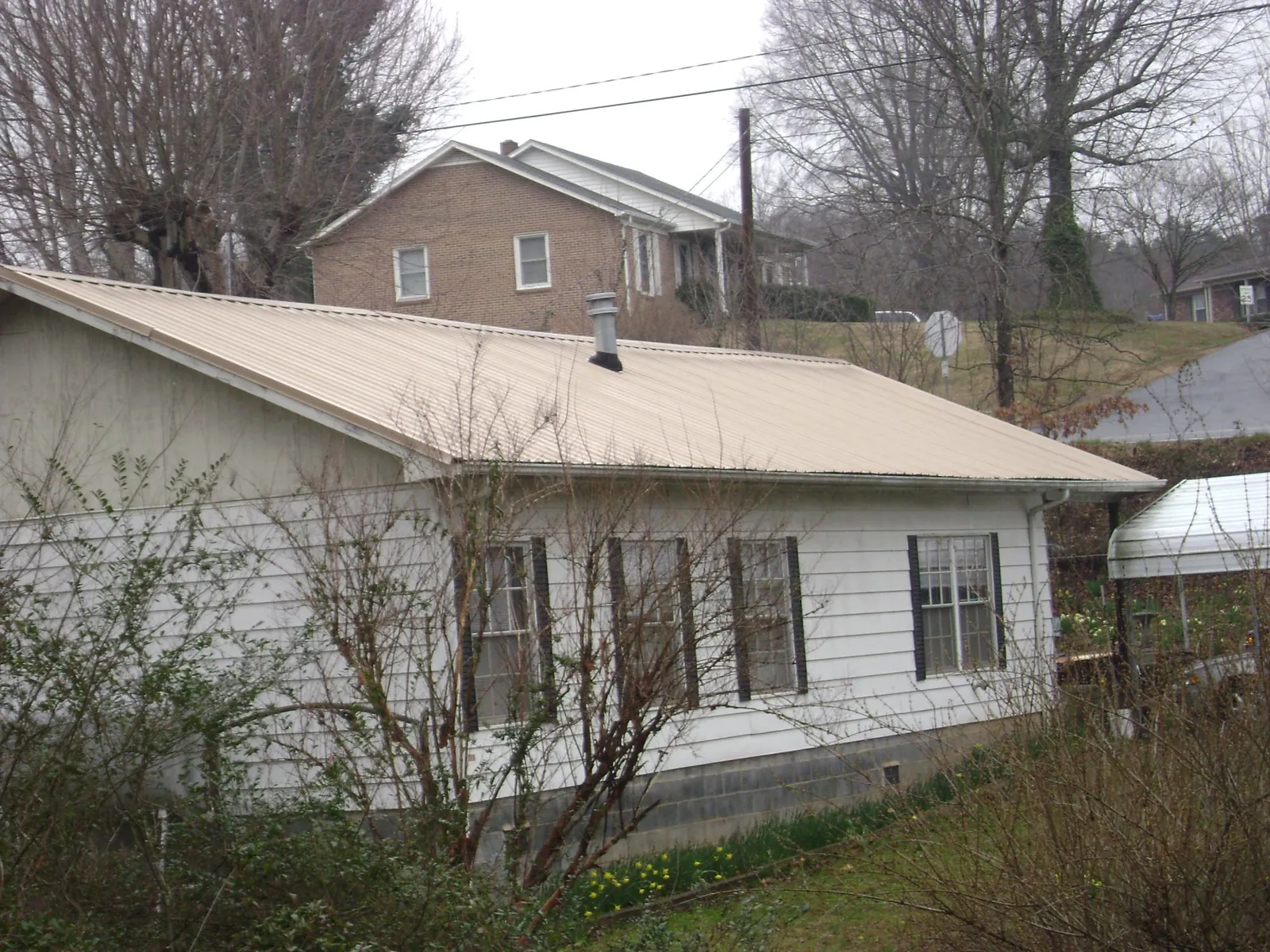 Tan metal roof on a white sided house set into a hillside — Commercial Roofing by Roofing Brothers in Bennet