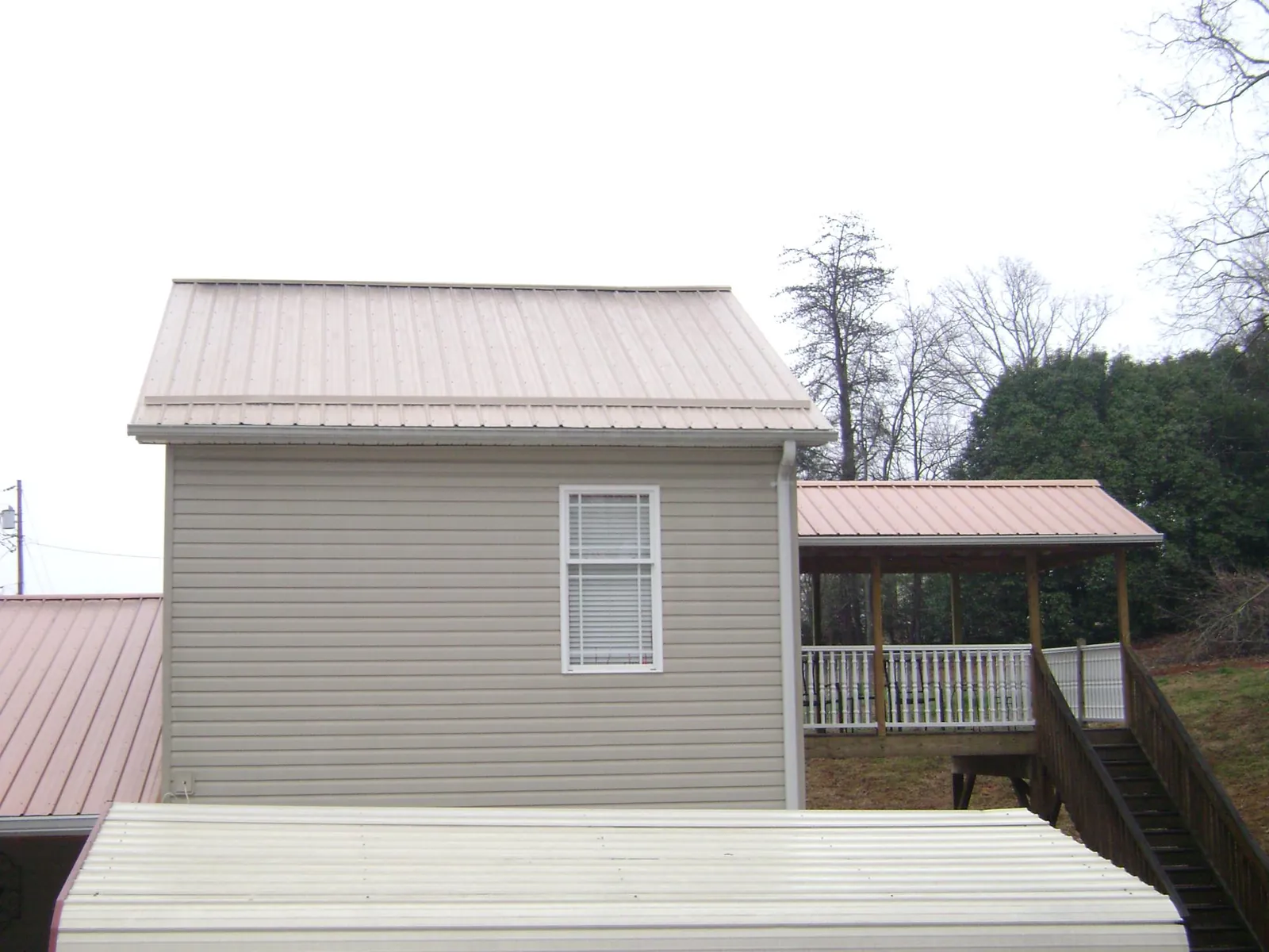 Tan metal roofs on a two story addition and attached porch, from a Roof Replacement job in Bennet